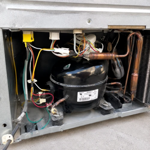 Rear panel removed from a refrigerator, showing the compressor, copper lines and wiring